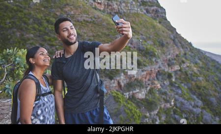 Hikes with you are always the best. a young couple taking photos while out on a hike in a mountain range outside. Stock Photo