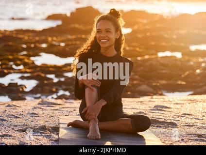 Yoga is the practice of being present in every moment. an attractive young woman sitting on her yoga mat during a yoga session on the beach at sunset. Stock Photo