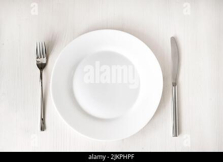 White clean plate and stainless knife and fork on light wooden table. Served cutlery. Top view Stock Photo
