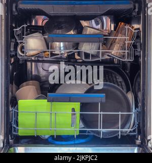 The dishwasher is filled with clean dishes after washing. Dishwasher with open door and washed plates and cups inside Stock Photo