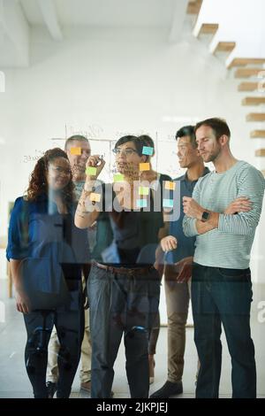 Diverse team of creative designers brainstorming and planning in an office together using sticky notes. Group leader and casual employees working on a Stock Photo