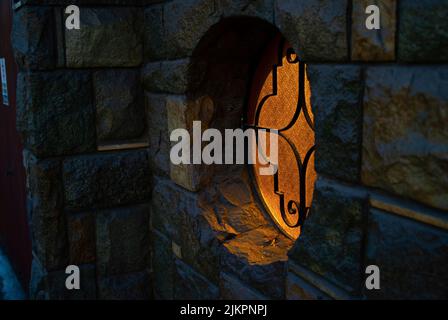 A view of a beautiful ornamented round window on a wall of a brick building with yellow light inside Stock Photo
