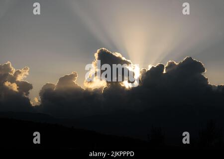 The sun rays through clouds and sunsets behind mountains Stock Photo
