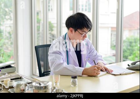 Asian doctor sitting at desk writing recording healthcare treatment on notebook Stock Photo