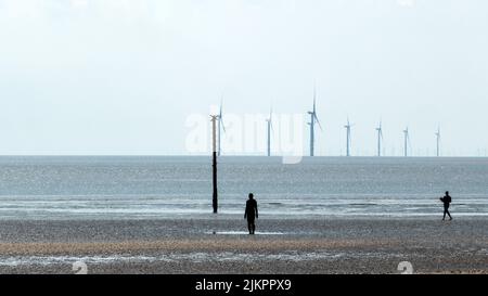 Two sculpture figures by the sea on Crosby Beach in England with wind turbines in the background Stock Photo