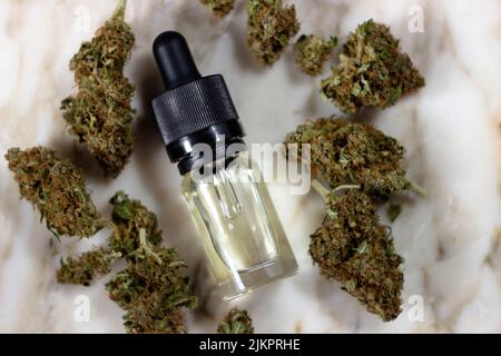 Medicinal cbd oil in a glass bottle with a pipette lies on a marble background surrounded by dry buds of medical marijuana of the honey peach variety Stock Photo