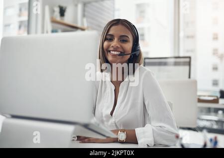 Lets change some frowns upside down, shall we. an attractive young businesswoman sitting alone in her office and wearing a headset while using her Stock Photo