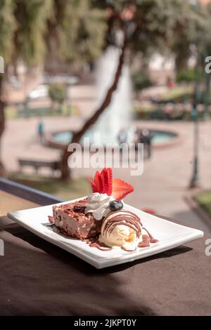A closeup of cake with ice cream and strawberry slices served in a plate on a blurry park background Stock Photo