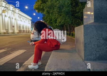 A plump woman with long curly dark hair in a bright red suit with a phone in her hands is sitting in the center of a European city at a pedestrian cro Stock Photo