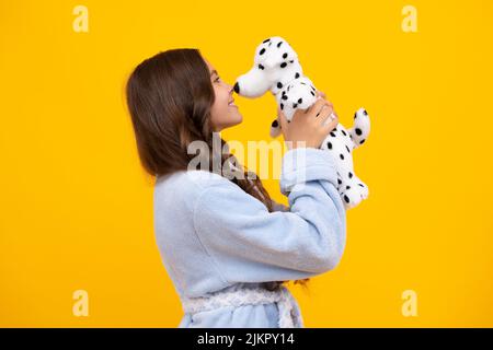 Child in pajamas, good morning. Teenager child girl in holding plush toy isolated on yellow background, happy childhood. Stock Photo