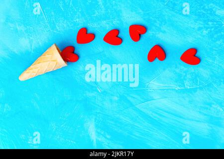 Small heart shapes and a waffle cone arranged on blue background with copy space. Stock Photo
