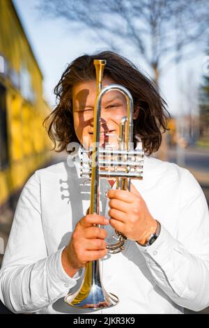 Young caucasian male cheerful jazzman looking through trumpet on sunny street Stock Photo