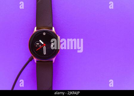 Smartwatch charging.Smart watch on wireless charging with on-screen charging indicator.Top view. Place for text.Blurred purple,veri peri color image b Stock Photo