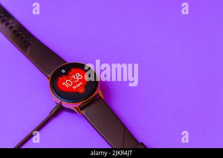 Smartwatch charging.Smart watch on wireless charging with on-screen charging indicator.Top view. Place for text.Blurred purple,veri peri color image b Stock Photo