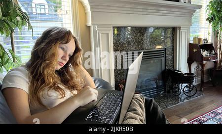 banner a lot of space for text Online learning knees with a laptopor watches a lesson She is sitting on a leather sofa next to a fireplace in her hands holding a laptop Vancouver Canada 07.2022 Stock Photo