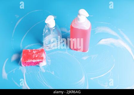 Spring cleaning. Soapy red sponge with two bottles of cleaning soap on foaming blue background. Stock Photo