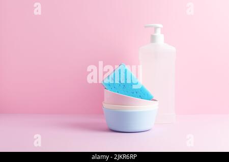Household cores. Clean plates, blue sponge and dishwash liquid on pastel pink background. Front view. Stock Photo