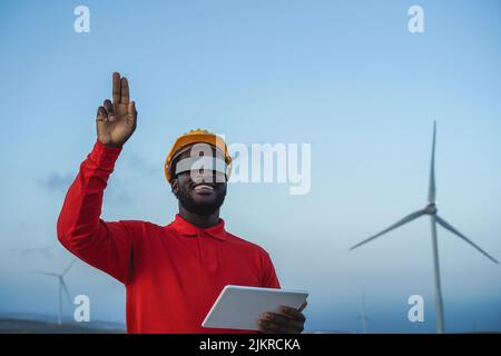 African engineer man using futuristic augmented reality glasses on a windmill farm - Focus on face Stock Photo