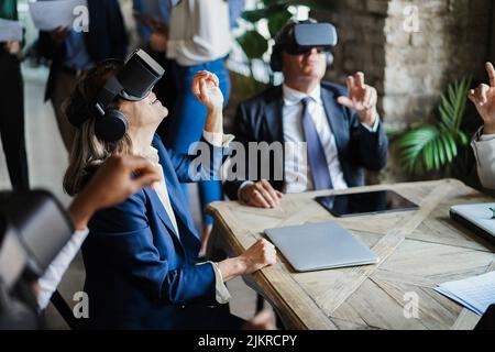 Business people wearing virtual reality goggles inside office - Focus on senior woman headset Stock Photo