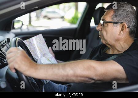 Senior behind the steering wheel of a car, looking at map for directions Stock Photo