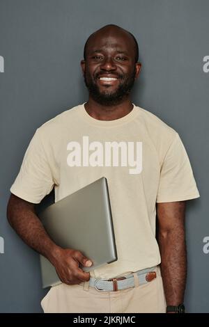 Portrait of African young businessman smiling at camera standing with laptop against the grey background Stock Photo