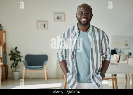Portrait of African young businessman in casual smiling at camera standing at modern office Stock Photo