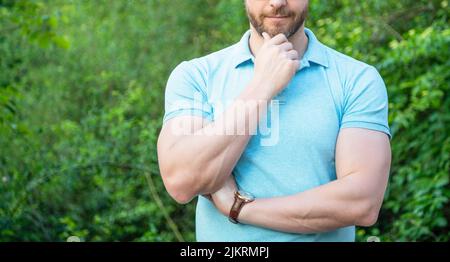 Handsome unshaven man crop view stroking chin natural background, copy space Stock Photo