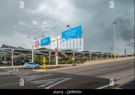 Vehicles arrive at Tucson International Airport next to parking lot. Directional signs display. Stock Photo