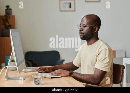 Serious African businessman in eyeglasses concentrating on his work on computer sitting at table at office Stock Photo