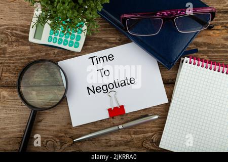Paper with text Time To Negotiate, notepad, eyeglasses, pen and magnifier on a wooden table. Flat lay composition Stock Photo