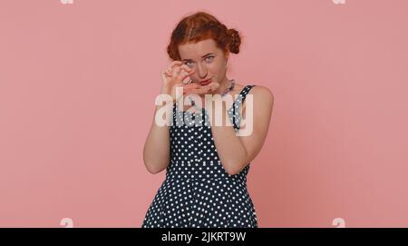 Need some more please give me. Woman showing a little bit gesture with sceptic smile, showing minimum sign, measuring small size asking for help. Ginger girl isolated alone on pink studio background Stock Photo