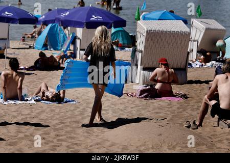 Berlin, Germany. 03rd Aug, 2022. A woman puts up a blue air mattress between the beach chairs on the sandy beach at Strandbad Wannsee. With temperatures around 33 degrees, many visitors are drawn to the outdoor pool. Credit: Carsten Koall/dpa/Alamy Live News Stock Photo