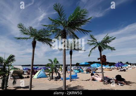 Berlin, Germany. 03rd Aug, 2022. Bathers lie out in the sun next to palm trees on the sandy beach at Strandbad Wannsee. With temperatures around 33 degrees, many visitors are drawn to the outdoor pool. Credit: Carsten Koall/dpa/Alamy Live News Stock Photo