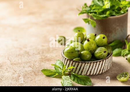 Fresh gooseberry in ceramic bowl with mint leaves on beige textured background with copy space Stock Photo