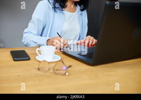 Senior woman designer using graphics tablet and stylus, working at laptop, using computer and digitizer at creative office Stock Photo