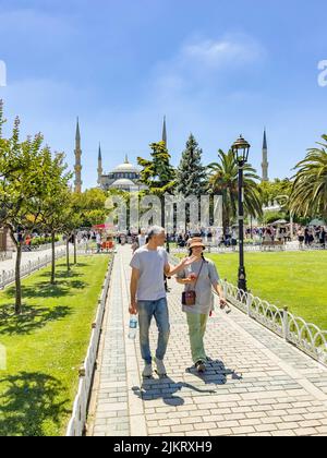 Istanbul - Turkey - July 14, 2022: Casual tourist couple walking in front of the famous blue mosque. Beautiful green public park with green palm trees Stock Photo