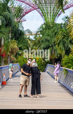 A Malay couple wearing sunshade is taking selfie pictures on the bridge before heading to Gardens by the Bay. Singapore 2022. Stock Photo