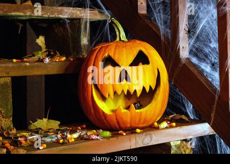 jack-o-lantern pumpkin and scattered Halloween candy on porch Stock Photo