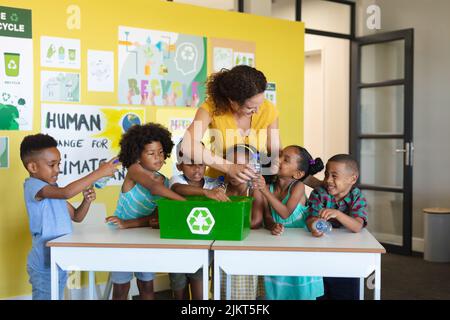 Multiracial elementary students and young female teacher collecting plastic bottles in container Stock Photo