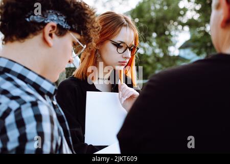 Close up of busy, engrossed group of people, two men and red haired woman in glasses do paperwork. Education, homework Stock Photo
