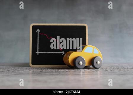 Toy car and chalkboard with downward arrow graph. Car rental dealer decrease lost sales concept. Stock Photo