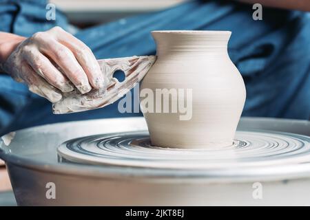 Woman hands working with tool on pottery wheel and making a pot. Stock Photo