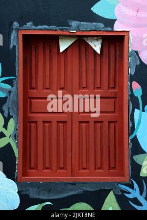 A closeup shot of a small window with red wooden window shutters on a colorful painted building Stock Photo