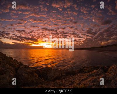 A beautiful scene of rocky beach by water against majestic sunset water with orange sunset sky Stock Photo