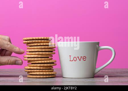 Hand taking a biscuit from a stack next to a mug with 'love' written on it. Stock Photo