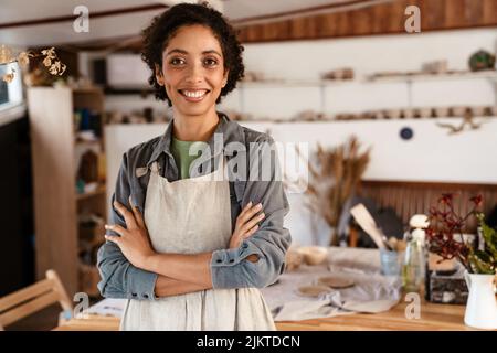 Young black ceramist woman wearing apron smiling while working in her studio Stock Photo