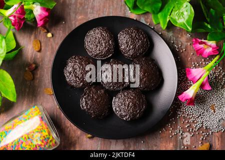 A top view of chocolate muffins on a black plate near decorative flowers and colorful candies Stock Photo