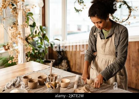 Young black ceramist woman wearing apron sculpting in clay at her workshop Stock Photo