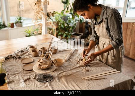 Young black ceramist woman wearing apron sculpting in clay at her workshop Stock Photo