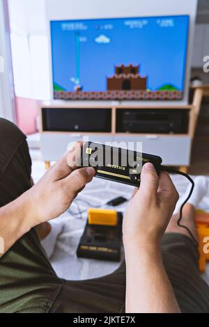 Male hands holding joystick from video-game console against background of home interior and TV-screen. First-person view. Home entertainment concept Stock Photo